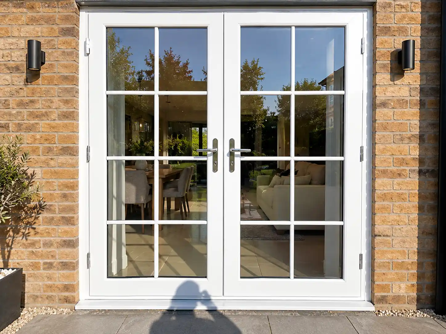 White double-glazed French patio doors with Georgian-style glazing bars on a brick house, with the photographer's shadow on the patio.